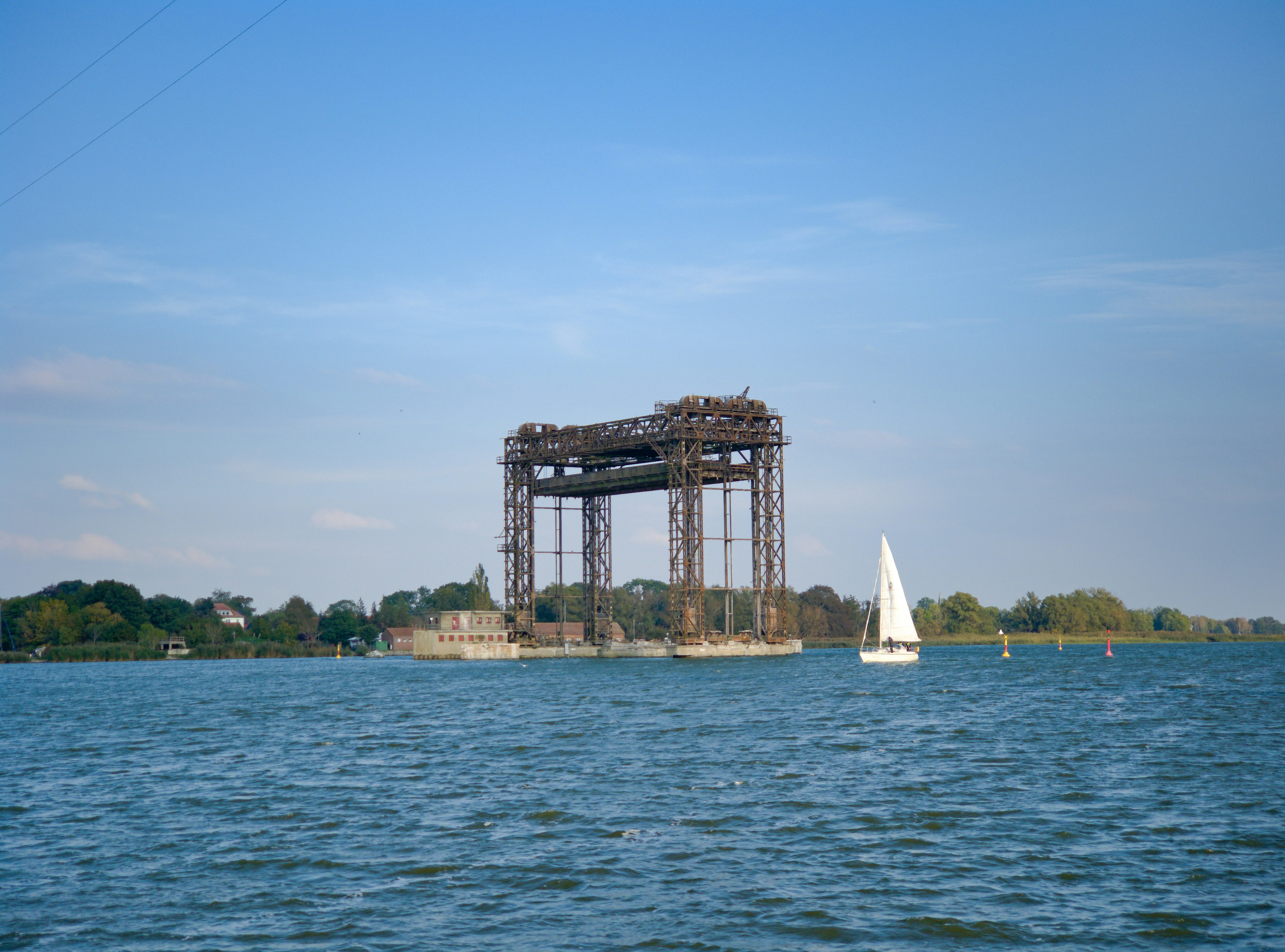 white sail boat on sea near brown concrete bridge under blue sky during daytime